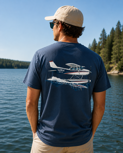 A man wearing a navy blue t-shirt with a large graphic of a seaplane on the back, standing by a lake with trees in the background.